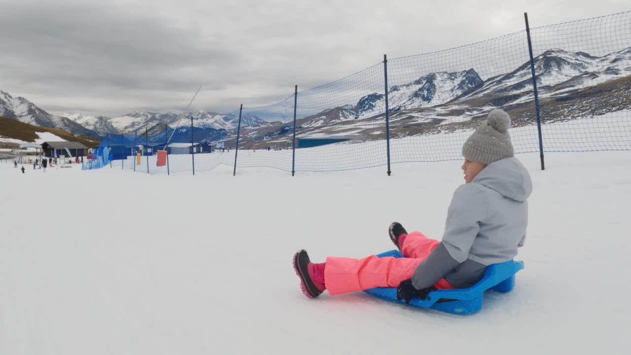 ребенок катается на санях в горах