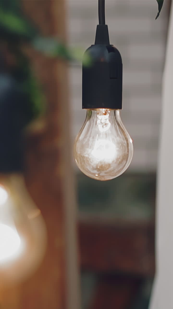 CU, slow motion: modern bright Edison light bulb hangs on ceiling in spacious restaurant hall against blurred background close view