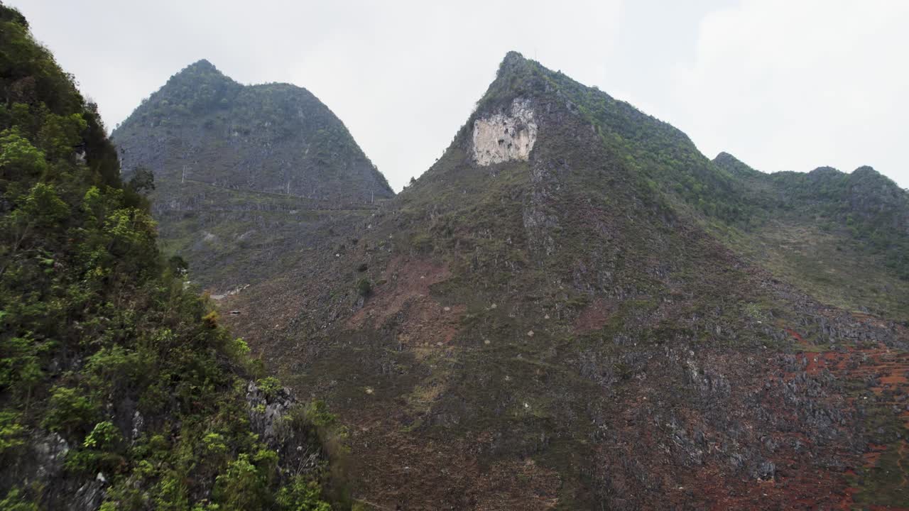 Lush green mountains in Northern Vietnam rise against a bright sky with rocky peaks in view