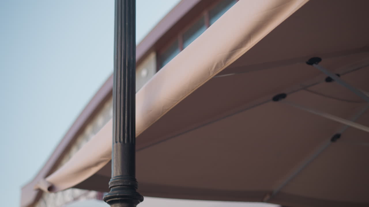 primer plano de un poste de lámpara negra que sostiene un dosel beige en un cielo brillante y despejado, los detalles arquitectónicos destacan el contraste entre los elementos urbanos y el entorno al aire libre pacífico