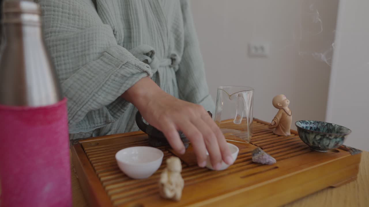A woman performs a tea ceremony with a teapot and teacups on a wooden tray