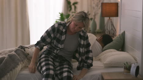 sad woman sitting on bed next to sleeping man