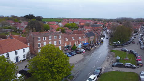 aerial drone shot flying through beautiful old village burnham market with people walking in street shopping on sunny and cloudy day north norfolk uk