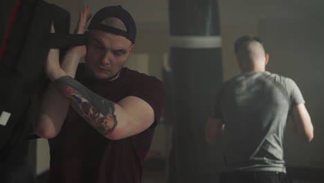 coach holds boxing gear for student to engage in boxing practice in dimly lit gym. fight club dedicated to practicing intense form of sport with guidance of trainer