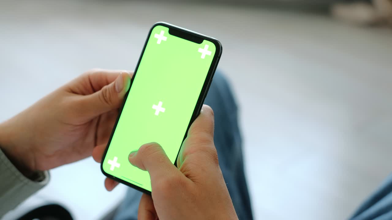 uomo seduto in poltrona a casa e utilizza uno smartphone con mock-up a schermo verde. 4k