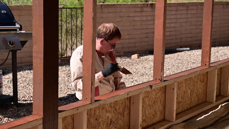 Male-House-Owner-Painting-Exterior-Of-A-Patio-Using-Paintbrush-Under-The-Sunlight