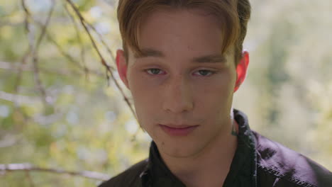 young tourist stands in forest, looks upward and shakes head slowly, winking eyes brow in tiredness. subtle sunlight filters through trees as exhaustion and contemplation show on his face