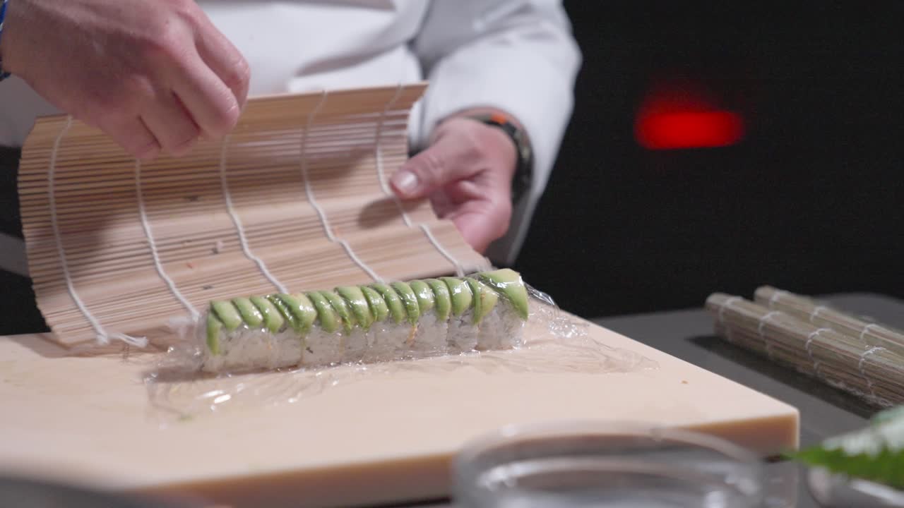 A static shot captures a sushi chef tightening a sushi roll with a straw mat, showcasing the technique and precision in sushi preparation. Perfect for culinary and sushi-making content.