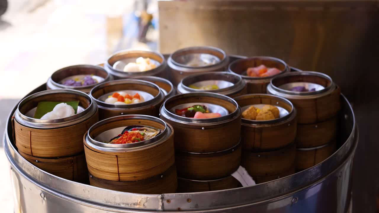 Hands arrange bamboo steamers filled with dim sum under natural lighting, capturing a culinary preparation moment