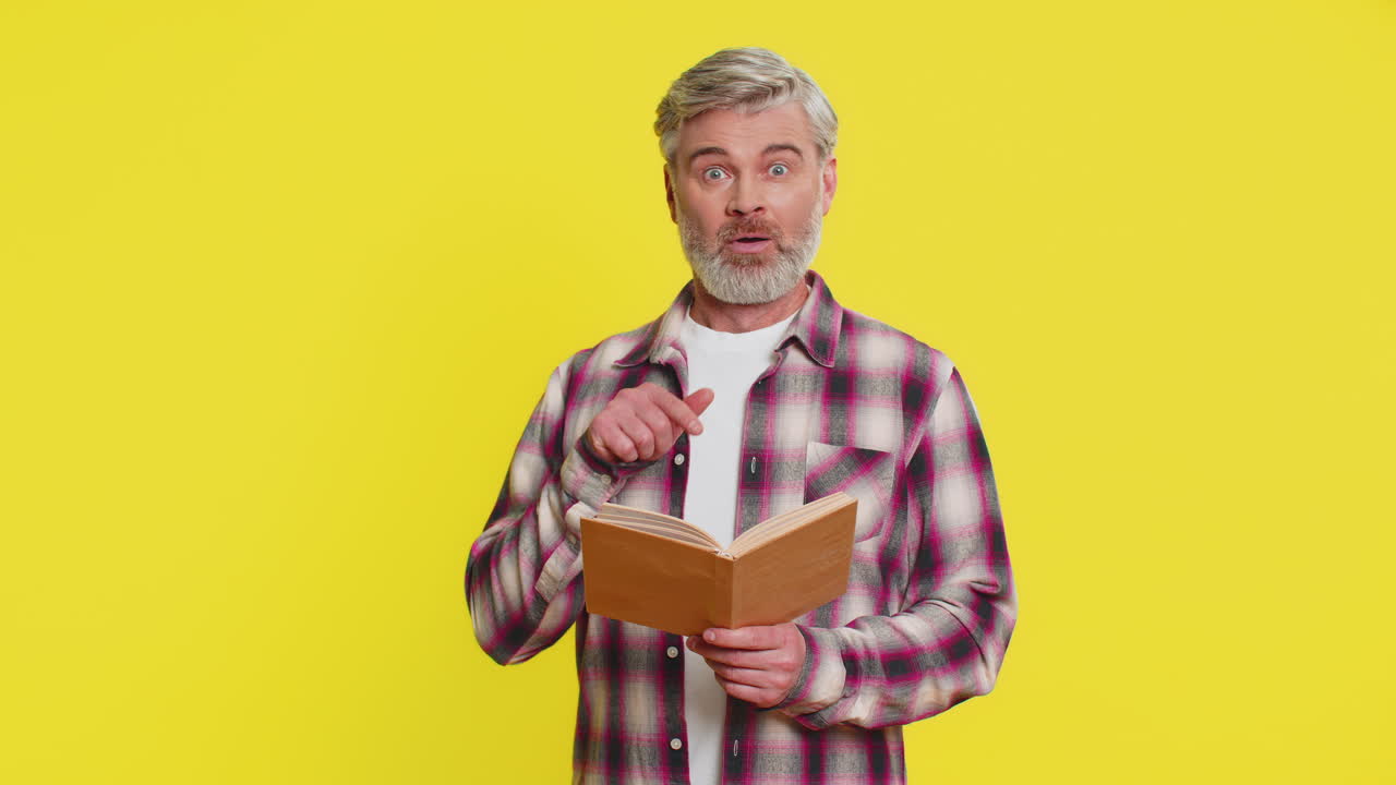 Mature man reading book in astonishment wideeyed surprise unexpected discovery wonder reaction