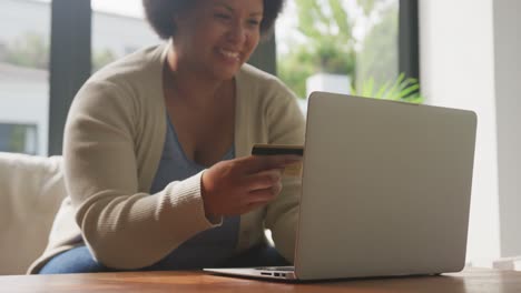 video of happy plus size african american woman holding credit card and using laptop