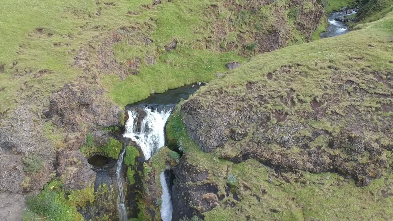 drone fly close to a natural waterfall with stone arch and green lush over the rock, fresh natural clean air in iceland