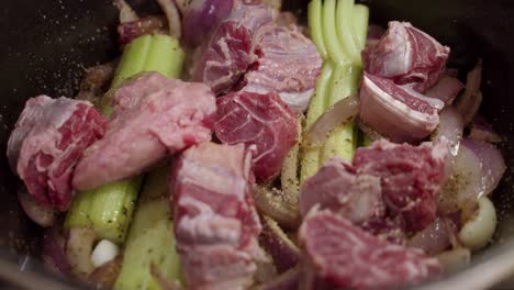 adding beef shank chops to onion slices, celery mixed with spices inside deep cooking pot