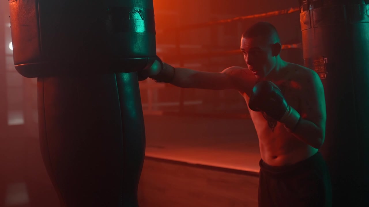 Pugile a torso nudo che si allena con un sacco da boxe in una palestra buia.