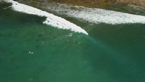 Shore-break-rolling-across-shallow-reef-in-Hot-Water-Beach,-New-Zealand-as-surfers-paddle-out-to-sea