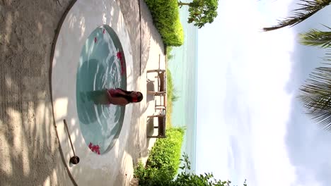 Young-woman-relaxing-in-a-hot-tub-with-red-flowers-floating-on-beach-front