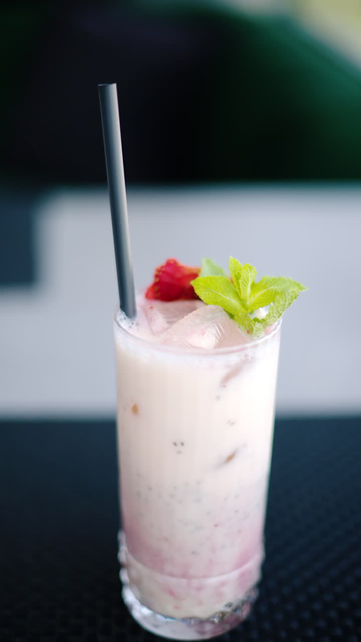 Una bevanda alla fragola con una cannuccia nera su un tavolo in un ristorante. Verticale