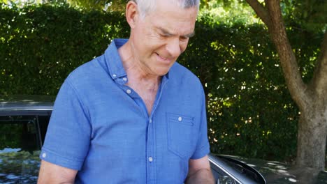 Senior-man-using-mobile-phone-near-car