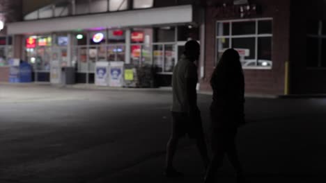 panning shot of a young couple walking past a gas station at night