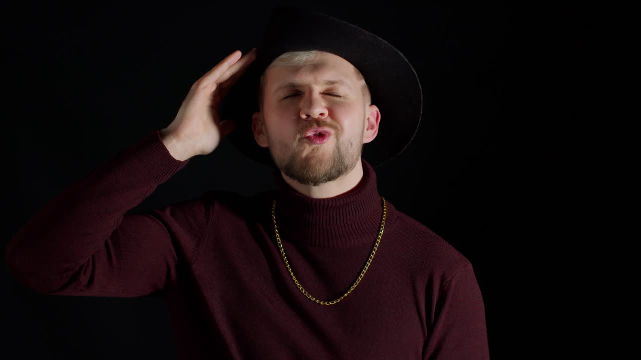 expresión facial de un hombre guapo con un sombrero elegante mirando a la cámara y sonriendo sobre un fondo negro