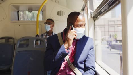 african american man in city wearing face, using smartphone in bus