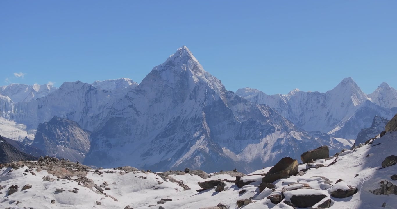 Everest-regionen, Nepal, luftfoto, der stiger forbi sneklædte forgrundsklipper for at afsløre den ikoniske nordvendte top af Mount Ama Dablam mod en klar blå himmel.