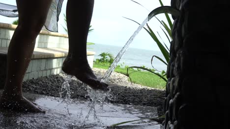 Frau-In-Zeitlupe,-Die-Füße-Mit-Wasser-Wäscht,-Nachdem-Sie-Strandpalmen-Und-Pool-Im-Hintergrund-Besucht-Hat