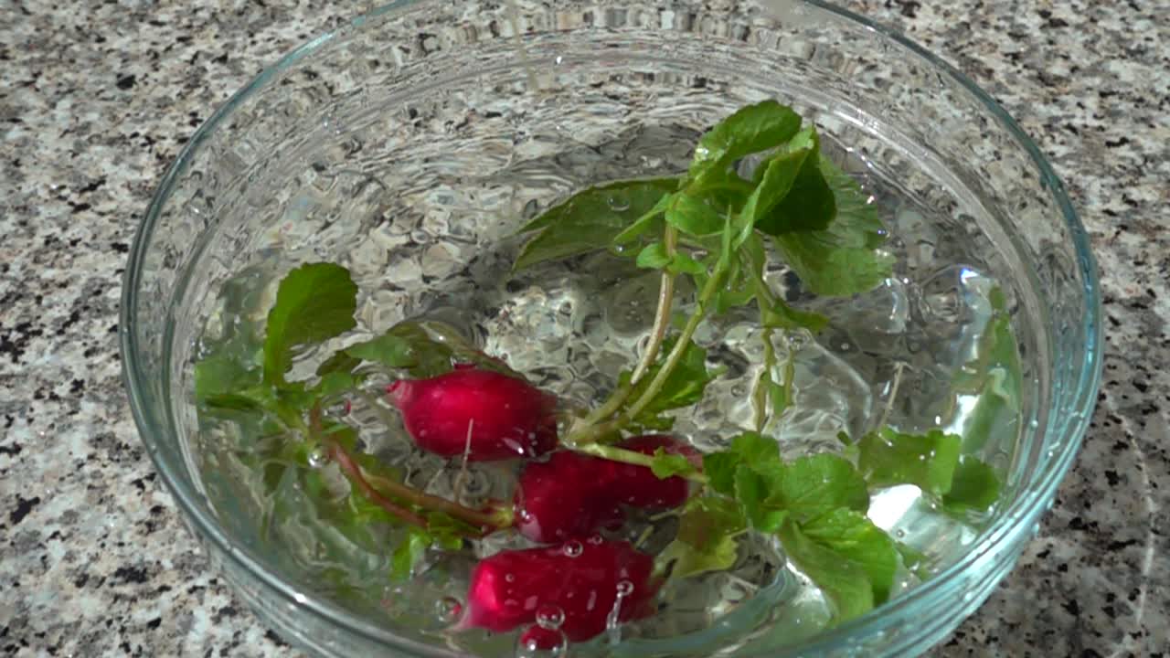 Caduta di ravanelli in una ciotola con acqua. Movimento rallentato.