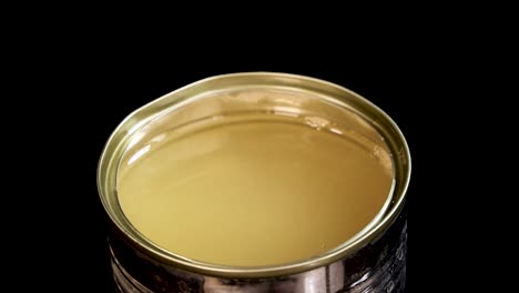 cooked green peas fall into an open can filled with liquid, creating splashes and bubbles. studio lighting highlights the metallic can against a black background