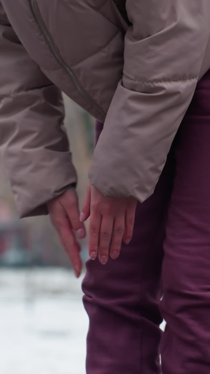 dama con traje de invierno inclinándose, sintiendo dolor en la rodilla y frotando la rodilla con árboles desnudos en el fondo, nieve en el suelo, mostrando incomodidad en un entorno invernal al aire libre frío