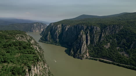 Impresionante-Vista-De-Dubova,-Rumania,-Que-Captura-El-Sereno-Río-Flanqueado-Por-Majestuosos-Acantilados-De-Piedra-Caliza,-Con-Un-Velero-Solitario-Deslizándose-Con-Gracia.