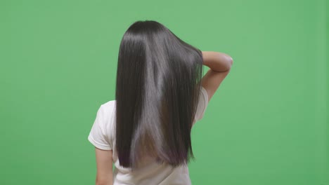 back view of a woman gently touching her long and black straight healthy hair in the green screen background studio