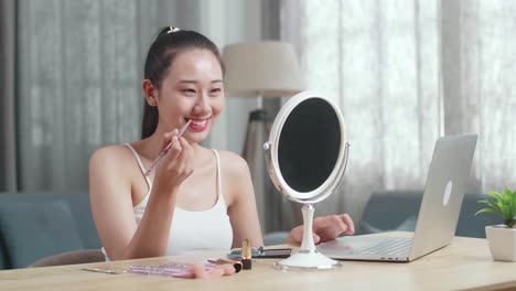 mujer aplicando maquillaje delante de la computadora portátil