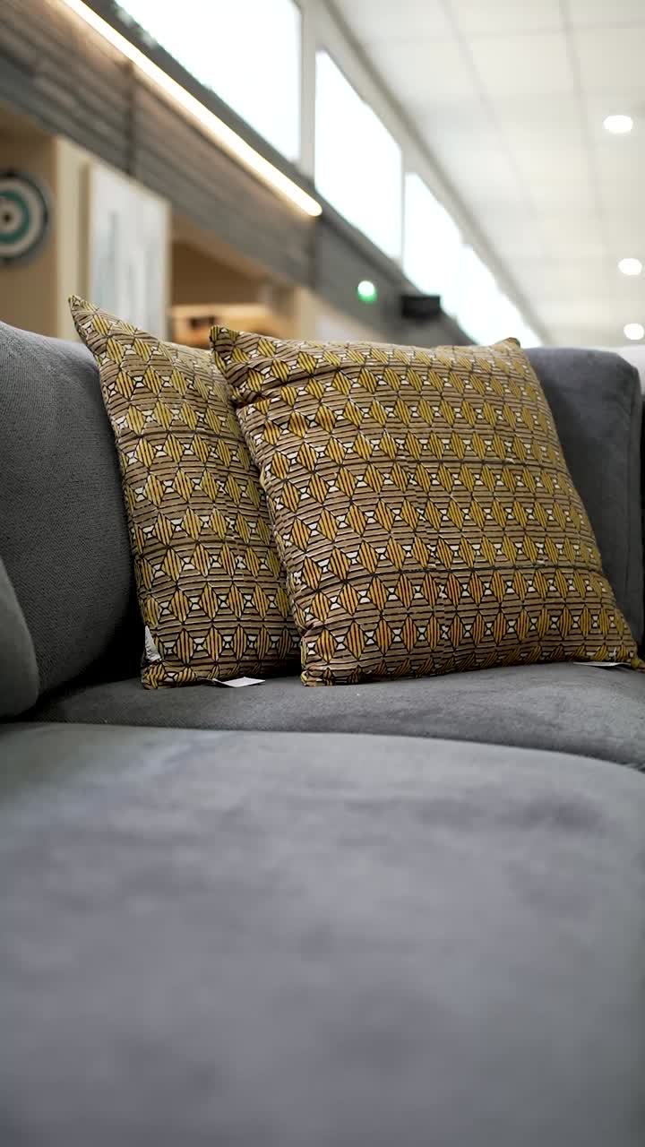 A cozy gray couch is adorned with vibrant patterned pillows, creating a warm atmosphere in a modern living area. The cozy setup invites relaxation and style