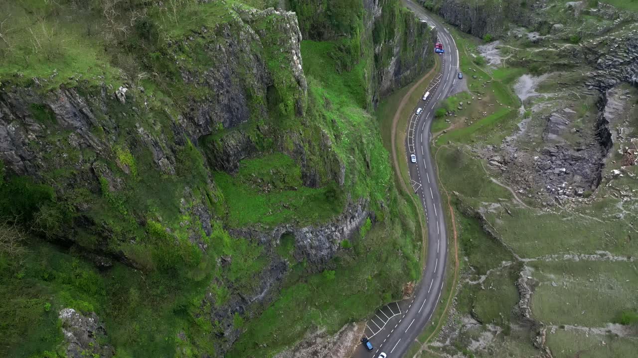 Locked-off aerial tilt-up showing limestone cliffs, winding road, and parked cars.