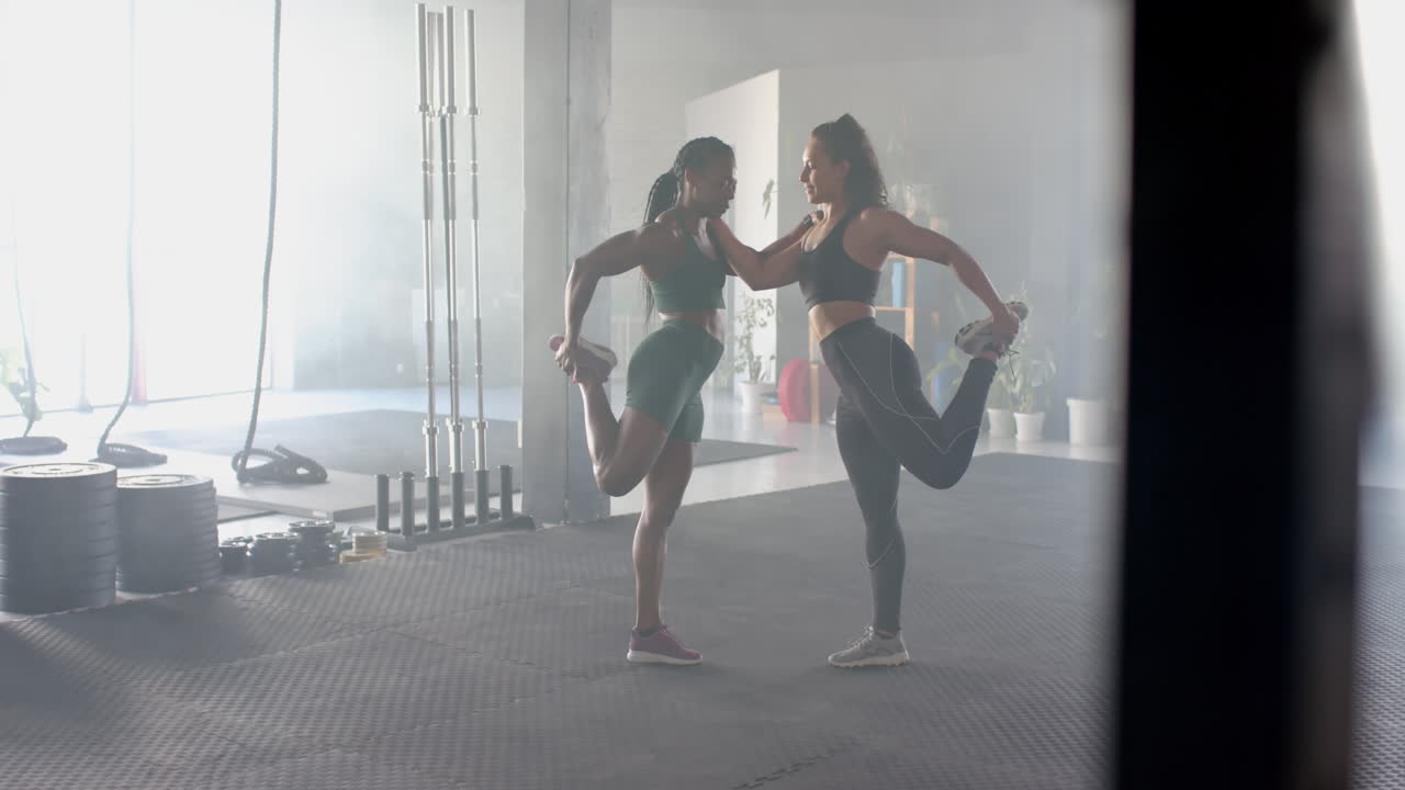 Stretching together, two women in gym wearing sportswear preparing for workout