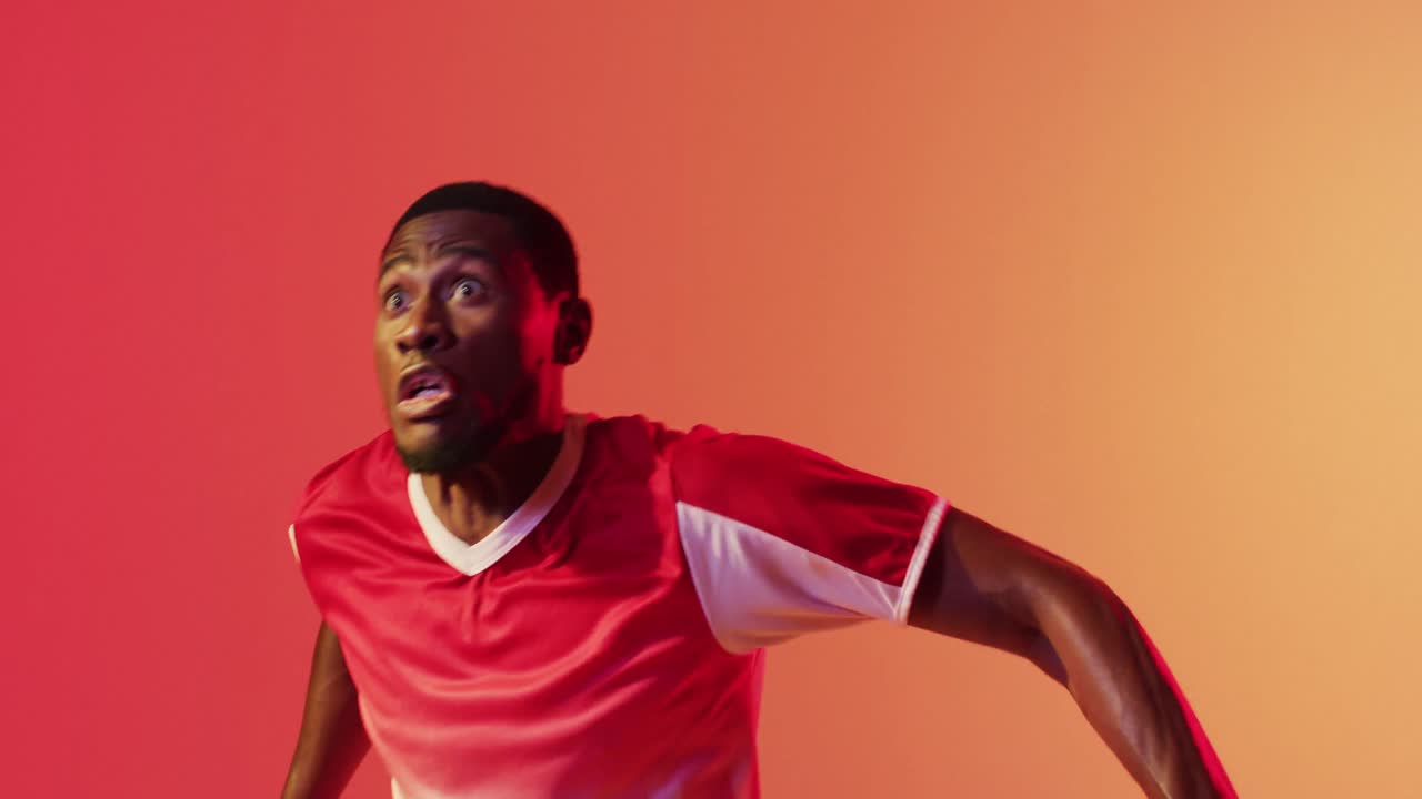 African american male soccer player returning football with head over neon pink lighting