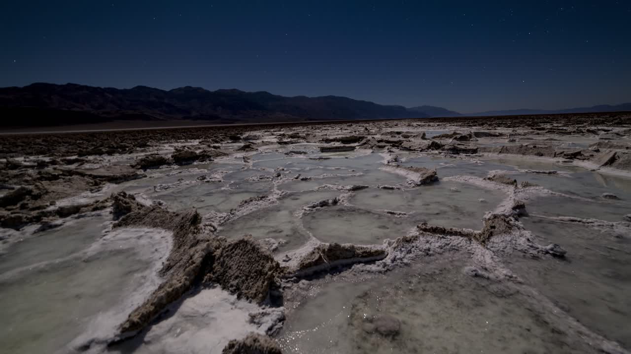 retroceder, panorámica de lapso de tiempo de formaciones de cristales de sal y piscinas de agua salada a la luz de la luna