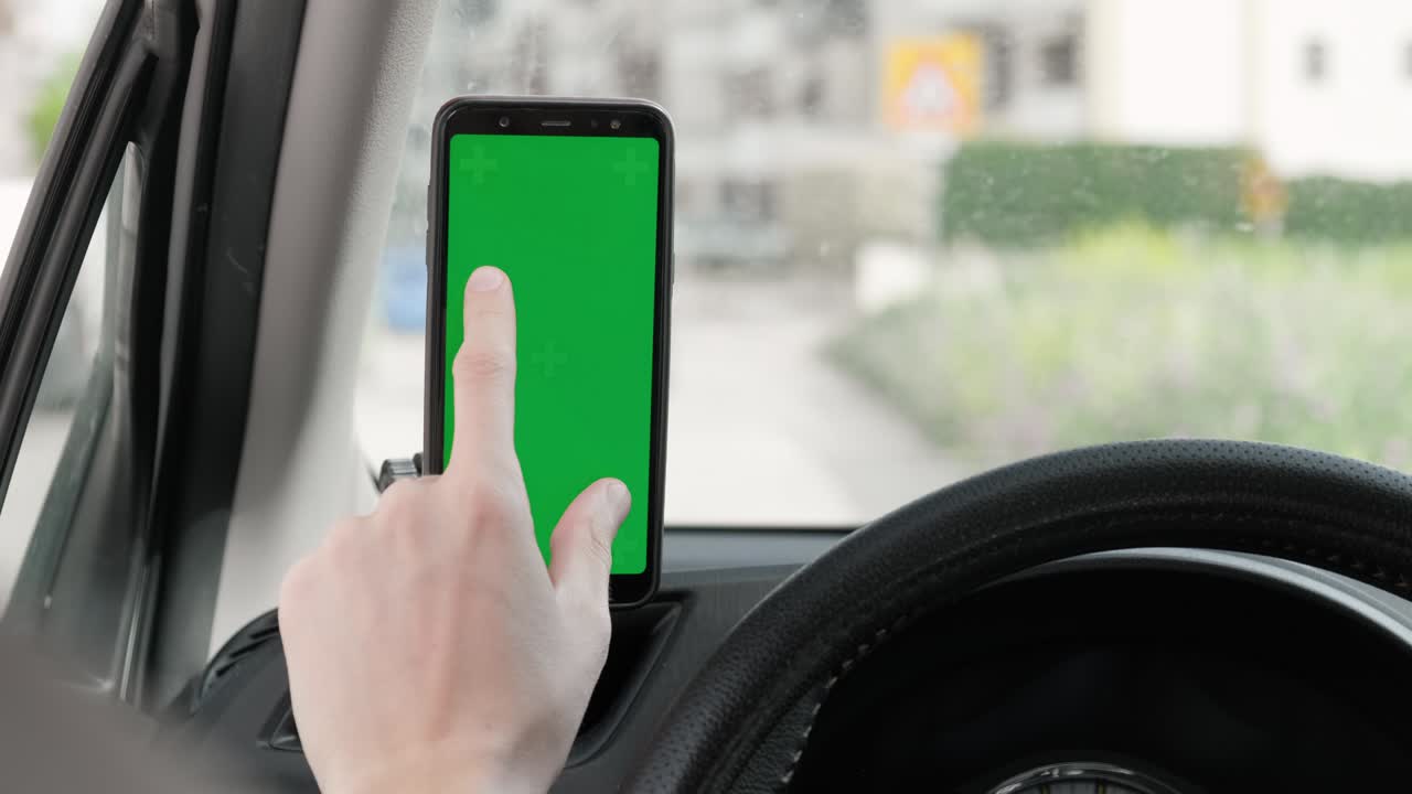 hombre tocando la maqueta de pantalla verde de su teléfono inteligente mientras conduce un coche.