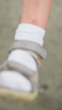 un primer plano de un niño con sandalias y calcetines blancos, balanceando rápidamente su pierna hacia adelante y hacia atrás