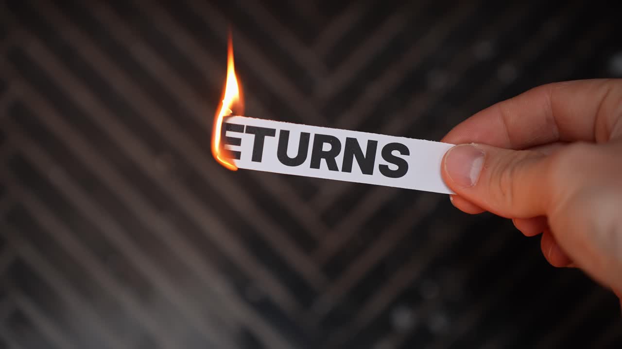 Hand burns a paper label reading “RETURNS,” symbolizing no-return policy—final sale, keep the purchase, and commitment to the deal. Dark background with copy space