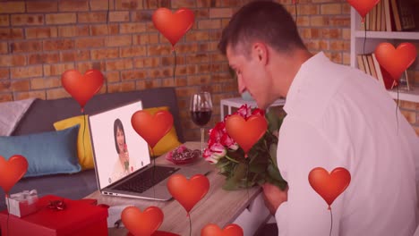 heart shaped balloons over caucasian man holding flower bouquet while having a video call on laptop