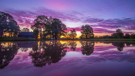 un amanecer sobre un paisaje con una cabaña en la orilla de un lago