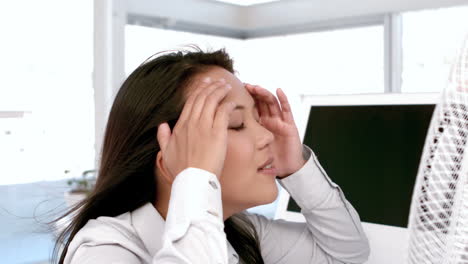 businesswoman enjoying cool air from the fan