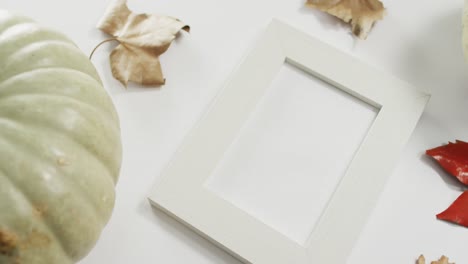 Empty-frame-with-copy-space,-pumpkin-and-autumn-leaves-against-white-background