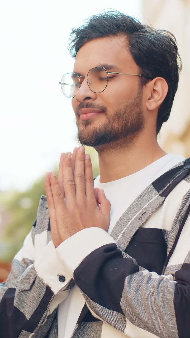 Religious indian man praying with closed eyes to god asking for blessing while standing on street