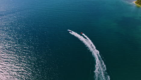 motorboat towing inflatable water ride in the blue sea leaving wake in the surface. - aerial shot