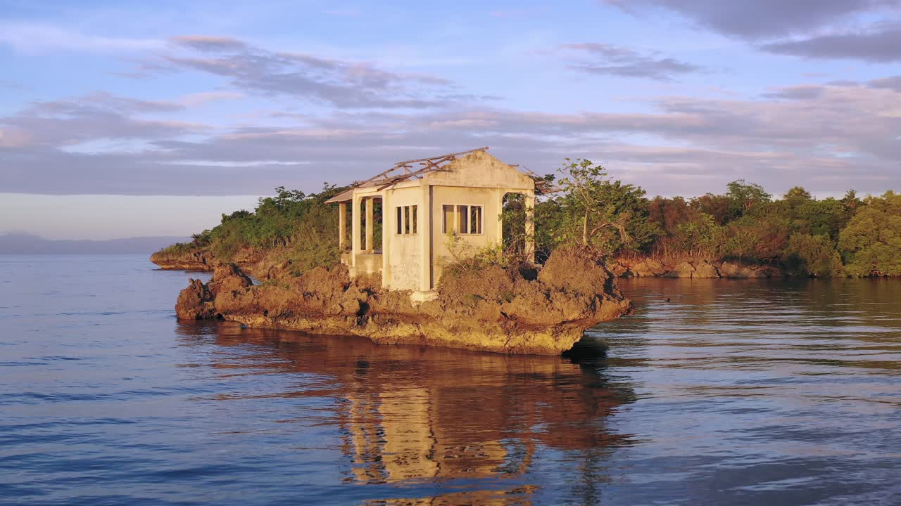 Low aerial drone over still ocean water towards dilapidated and abandoned building