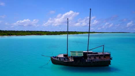 Traditional-Maldivian-ship-anchored-in-bright-turquoise-lagoon,-Aerial-pan-4k