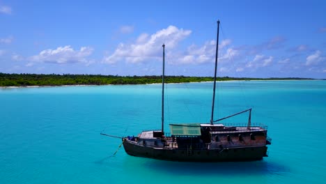 traditional maldivian ship anchored in bright turquoise lagoon, aerial pan 4k